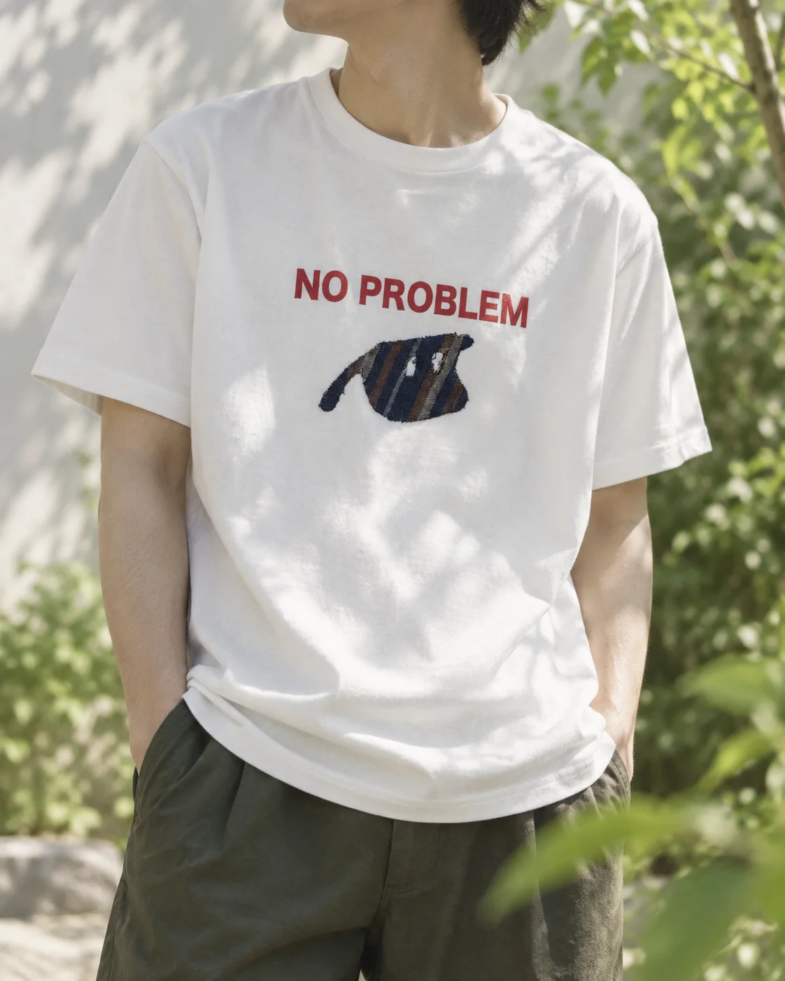 A person wearing a white Namakemono T-shirt in dappled sunlight